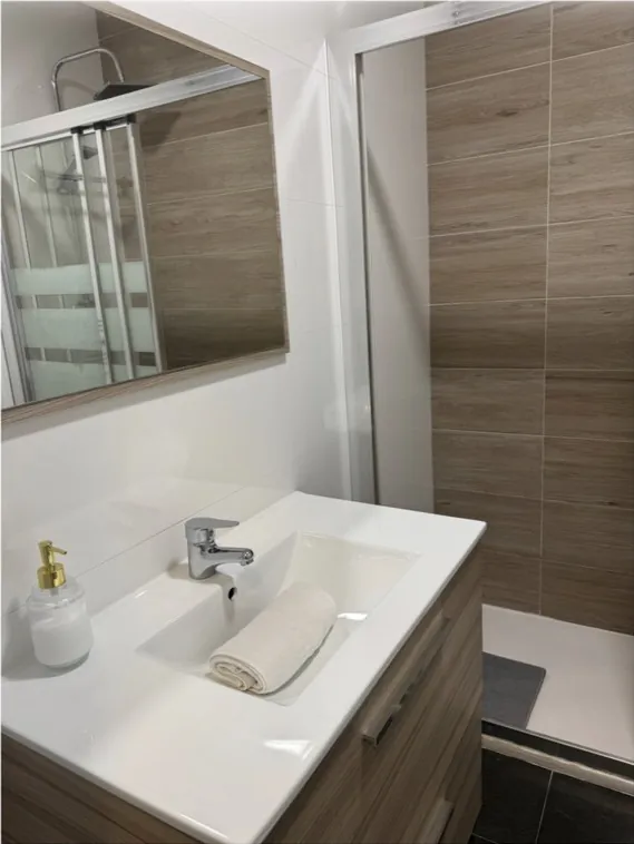 Baño con lavabo blanco, espejo y ducha limpios
